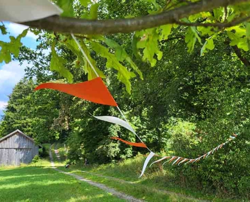 Eine an einen Baum gespannte Wimpelkette flattert auf einer Wiese im leichten Wind