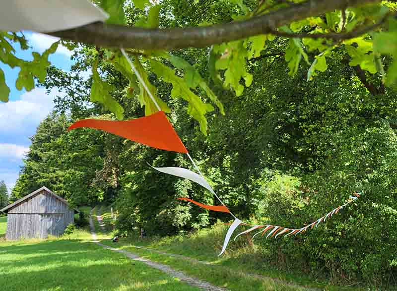 Eine an einen Baum gespannte Wimpelkette flattert auf einer Wiese im leichten Wind