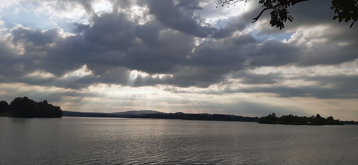 Sonne strahlt hinter Wolken versteckt über einen See